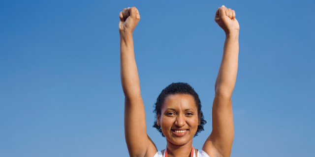 Mulher sorri com os braços erguidos acima da cabeça.