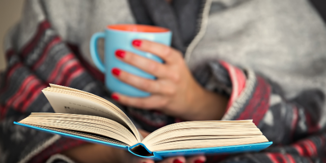Mulher segura caneca e lê livro.