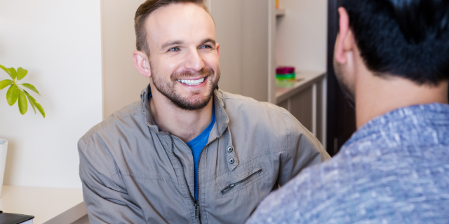 Dois homens conversam. Um deles sorri.