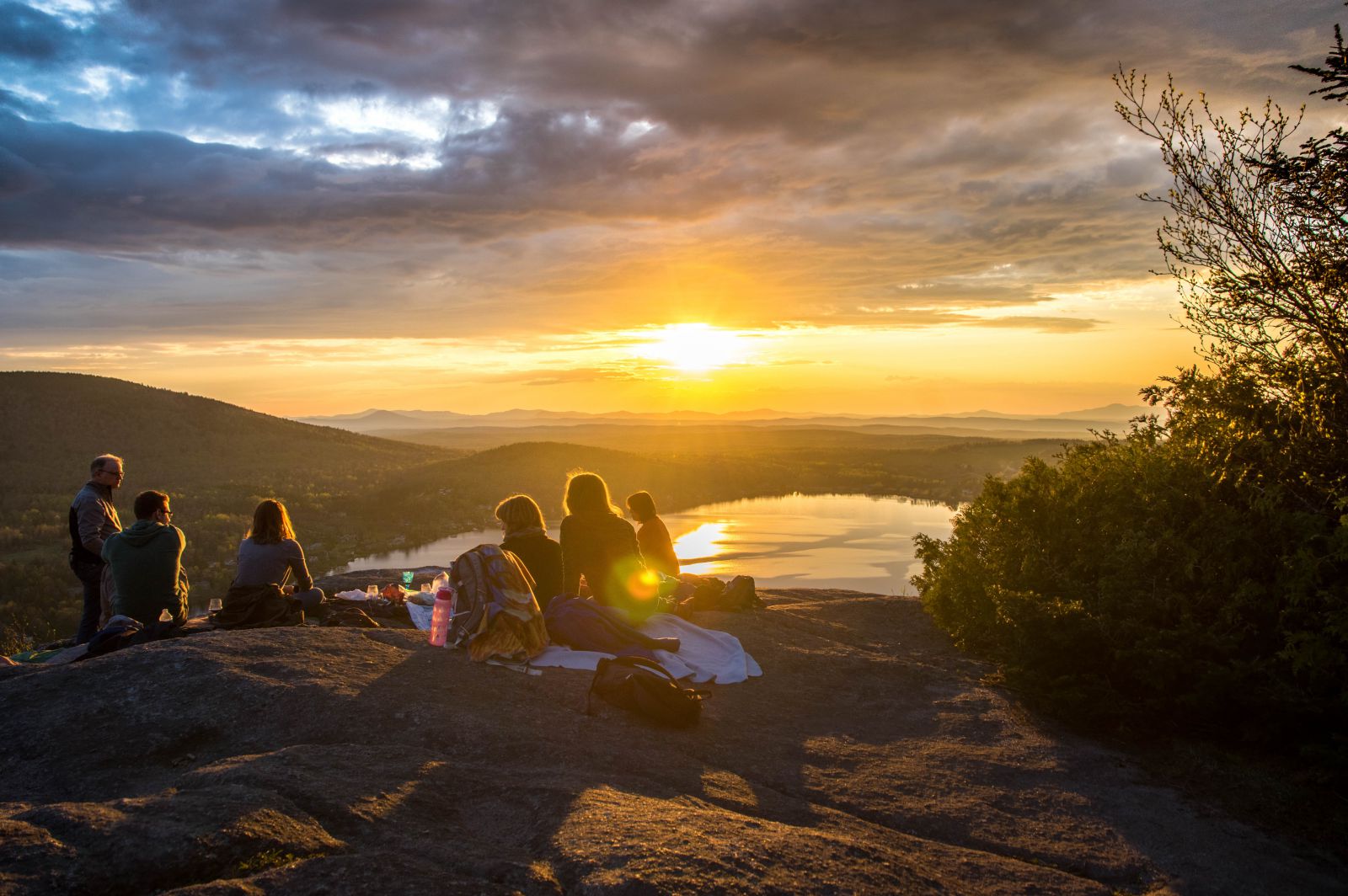 Amigos fazendo um piquenique sobre um pico ao pôr do sol.