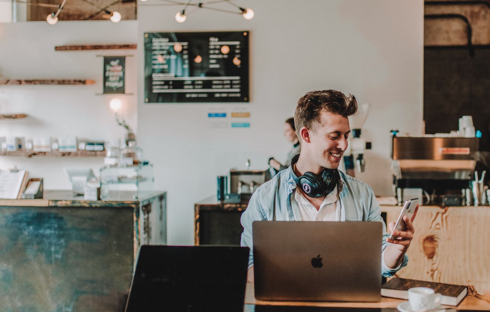 Homem sentado em um café com um computador e um celular