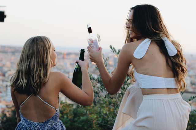 Mulheres brancas brindando com garrafas.
