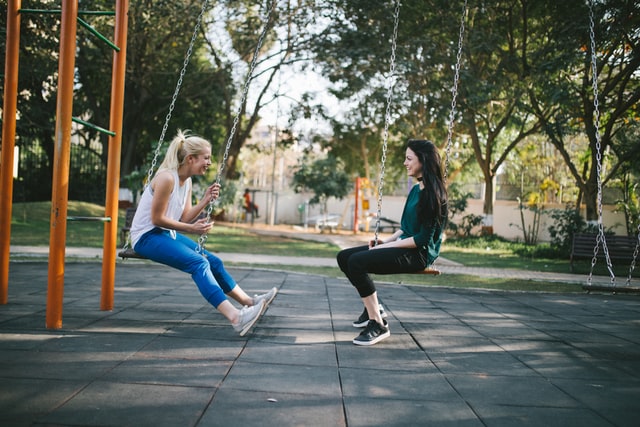 Mulheres brancas sentadas em balanços conversando.