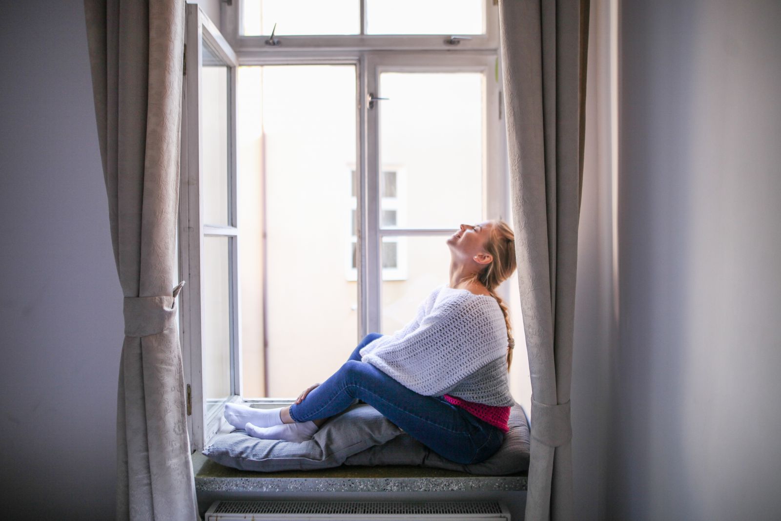 Mulher sentada em sua janela sorrindo e olhando para cima