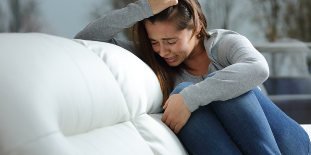 Garota chora sozinha sentada em sofá branco.