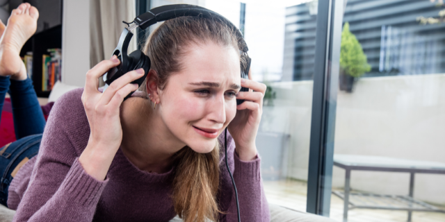 Mulher deitada de bruços chora. Ela está com fones de ouvido. 