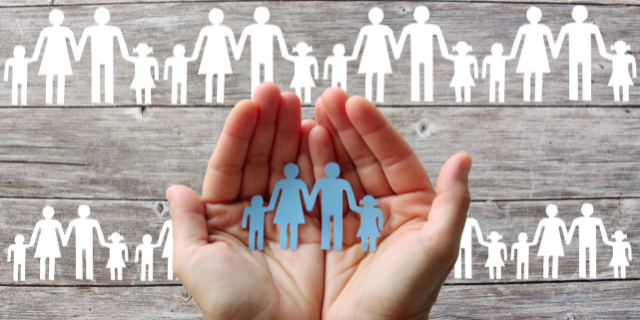 Duas mãos seguram uma família recortada em papel. Ao fundo, há uma superfície de madeira clara e outras representações familiares.