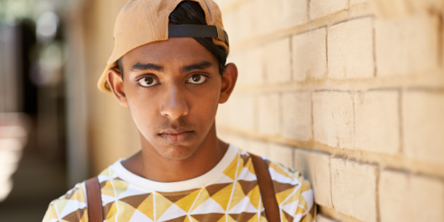 Menino de boné com olhar fixo ao centro da imagem. 