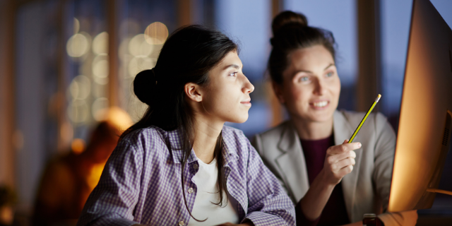 Duas mulheres observam a tela de um computador. 