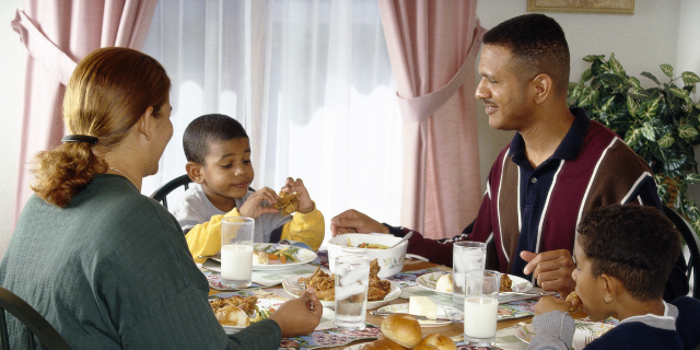Família sentada à mesa tem refeição.