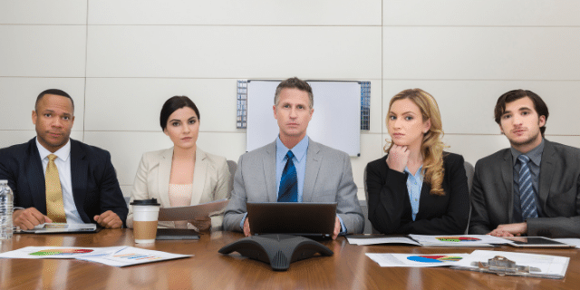 Cinco pessoas sentadas em uma mesa sérias. 