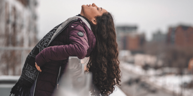 Mulher com as costas apoiadas em grade de uma sacada. Ela está com os olhos fechados e a cabeça inclinada para trás.