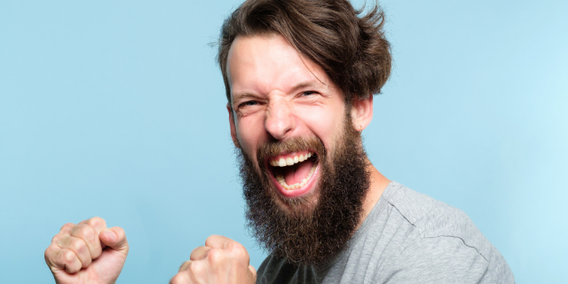 Homem com as mãos erguidas sorri e comemora. O fundo no qual ele está é azul claro.