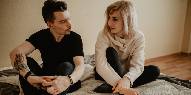 Homem e mulher sentados em uma cama olham um para o outro.