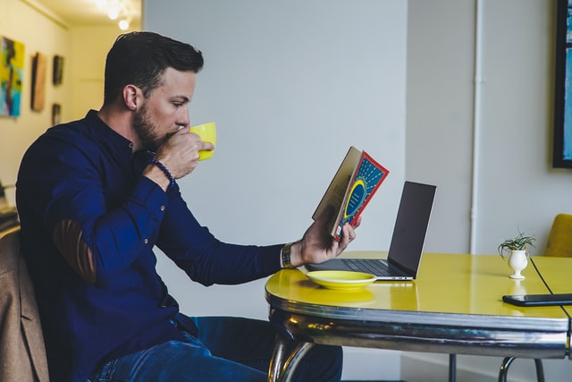 Homem branco segurando livro e caneca amarela.