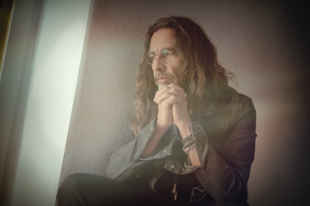 Homem branco de cabelos longos e expressão pensativa.