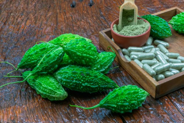 Pequenos melões de São Caetano amontoados. Ao lado, um punhado de cápsulas e um pequeno pote com pó, ambos feitos com a fruta.