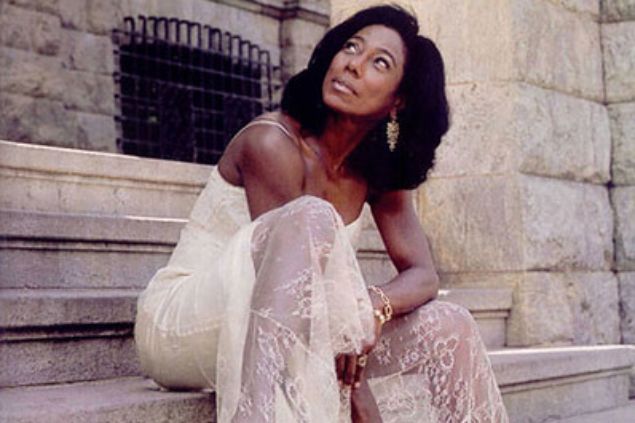 Gloria Maria sentada em uma escada e olhando para cima