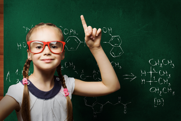 Menina com óculos e com a lousa atrás cheia de fórmulas químicas