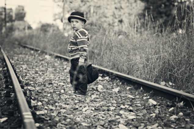 Menino no trilho de trem com uma mala olhando para trás