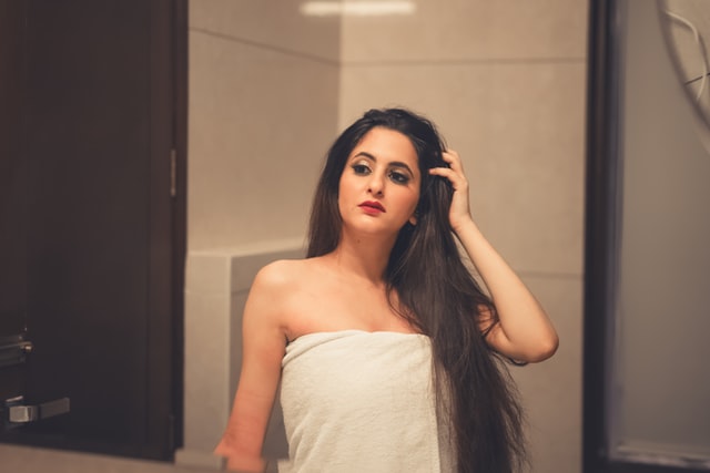 Mulher branca enrolada numa toalha branca, olhando-se no espelho com olhar determinado.