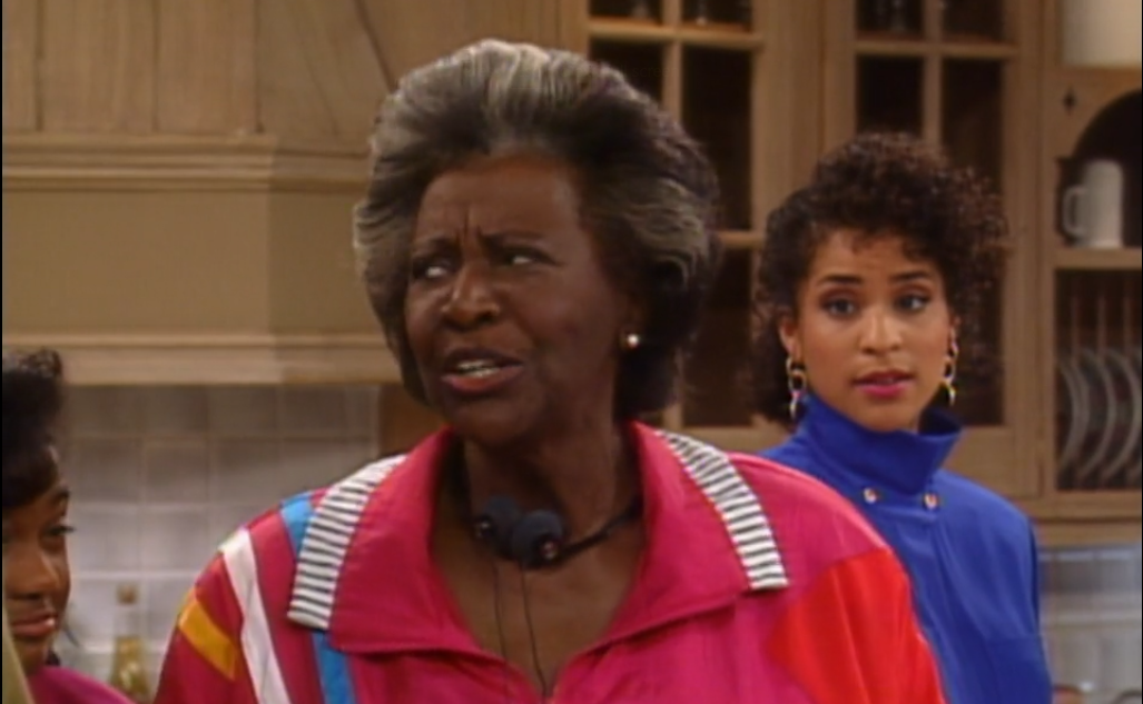 Mulher negra de cabelos curtos e grisalhos usando camisa rosa.