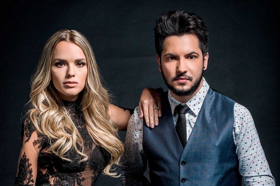 Thaeme e Thiago em um fundo escuro olhando para frente com seriedade 