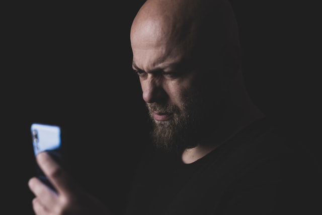 engin akyurt / Unsplash Homem branco segurando celular com expressão brava.