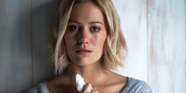 Mulher chora segurando lenço próximo do colo.