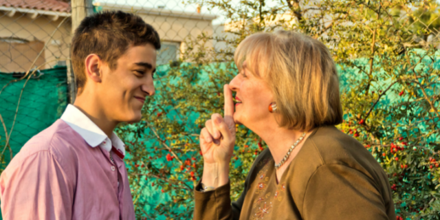 Avó e neto sorriem. Ela ergue o dedo indicador. 