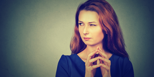 Mulher bate os dedos de uma mão contra os da outra. Ela olha para o lado com os olhos semicerrados.