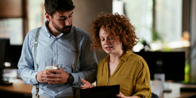 Homem e mulher conversam enquanto olham para prancheta.
