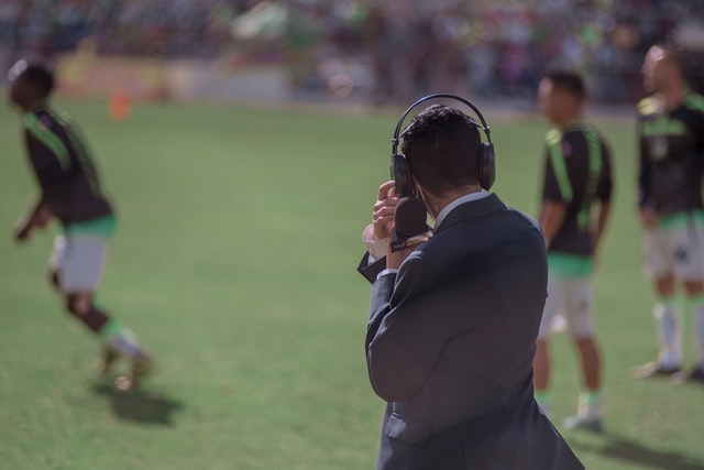 Homem branco com fones num campo de futebol.