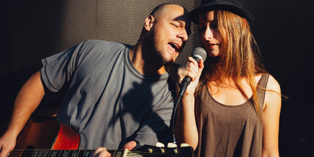 Um homem e mulher cantam juntos. Ele está tocando um violão.