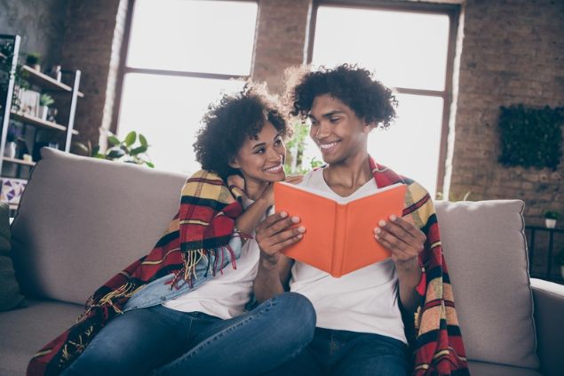 Casal apaixonado lendo um livro juntos, sentados no sofá.