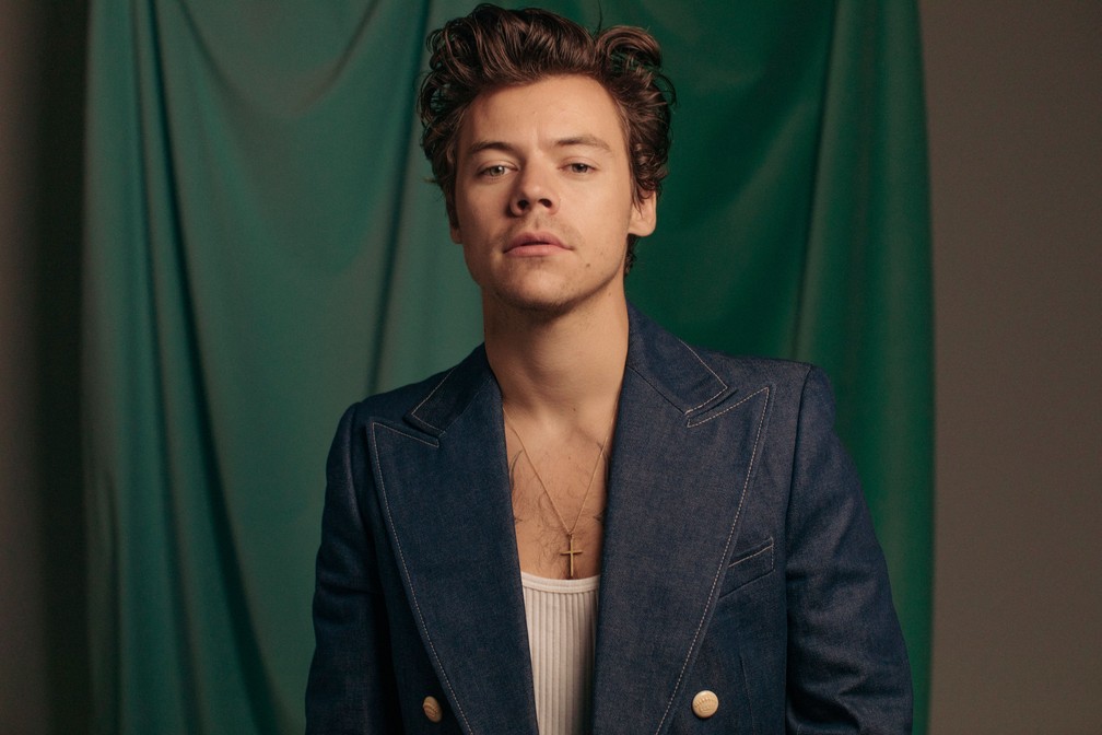 Harry Styles em sessão de fotos, com camiseta regata cavada e blazer jeans.
