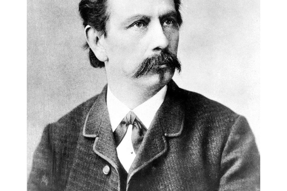Karl Benz usando terno e olhando para o lado com seriedade