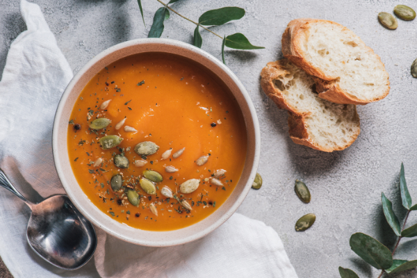 Sopa de moranga em um bowl, ao lado de pães e talheres