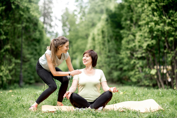 Mulher auxiliando uma idosa sentada em um tapete de yoga