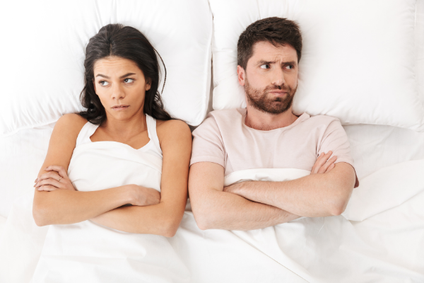 Mulher e homem irritados deitados na cama, de braços cruzados