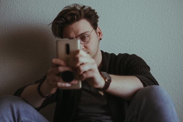Joshua Reddekopp / Unsplash Homem branco segurando celular com expressão brava.