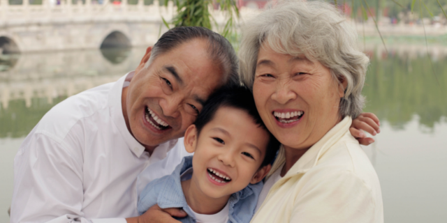 Neto entre os dois avós. Os três sorriem.