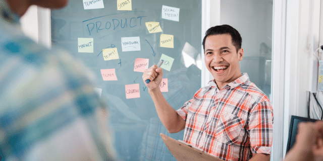 Um homem feliz apontando para um mural cheio de post-it.