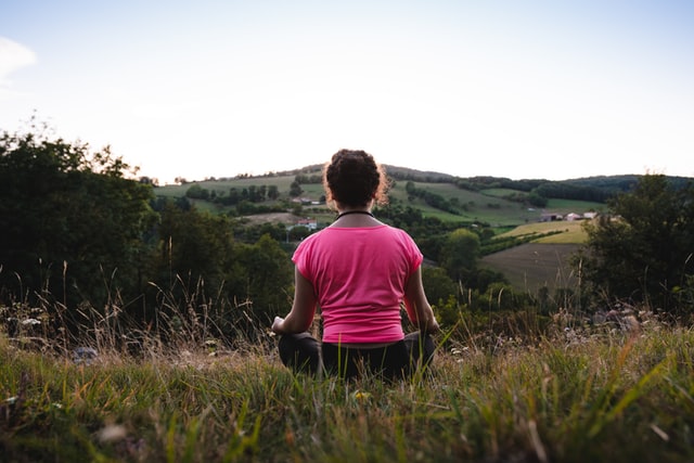 Mulher branca meditando num campo.