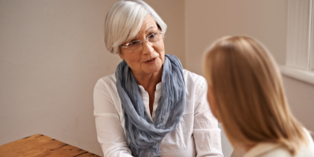 Avó e neta sentadas à mesa; elas conversam.