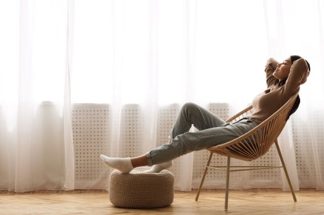 Mulher sentada relaxadamente em uma cadeira, com os pés apoiados em um pufe.