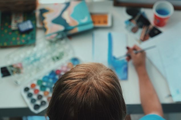Visão de cima de uma pessoa fazendo arte com tintas coloridas sobre uma superfície.
