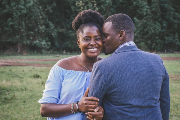 Casal abraçado com mulher de frente sorrindo e beijando seu rosto