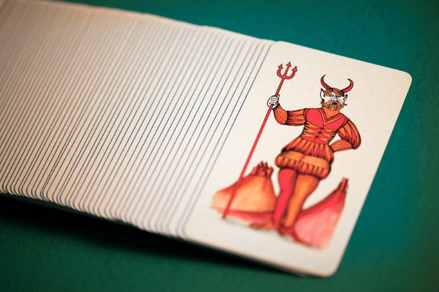A carta O Diabo do Tarot está em destaque sobre uma mesa. Embaixo, há outras cartas de Tarot.