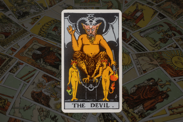 Montagem com a carta O Diabo do Tarot na posição normal. Ao fundo, há várias cartas de Tarot.
